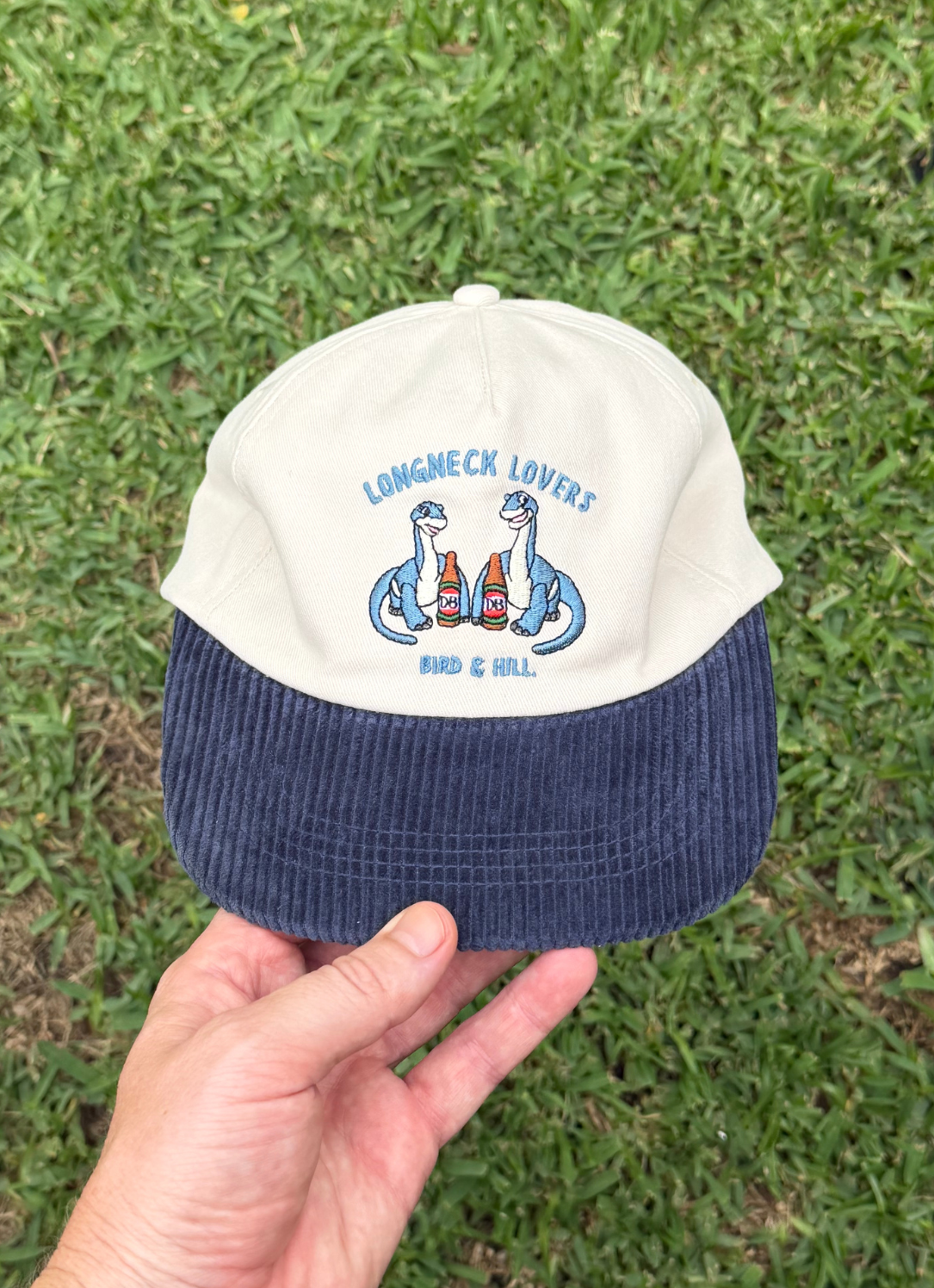 Bird & Hill Longneck Lovers 5 Panel hat worn in a lifestyle setting, featuring dinosaur lovers drinking longneck beers. 